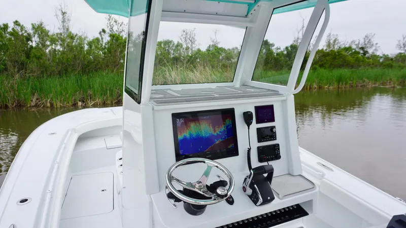 Slide: The Image of 2022 Costa Custom Boats 264 HC helm with advanced navigation system, steering wheel, and lush greenery backdrop. - 26