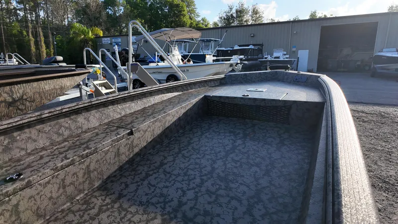 Slide: The Image of 2025 Xpress H18DB boat with textured interior, parked outdoors near other boats. - 22