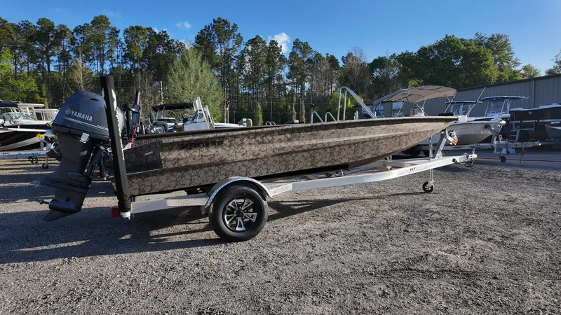 Slide: The Image of 2025 Xpress H18DB boat on trailer, parked outdoors with trees in background. - 9