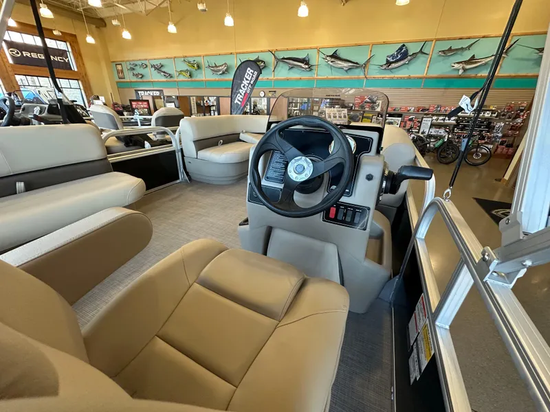 Slide: The Image of 2025 Sun Tracker Party Barge 16 DLX interior with beige seating and steering wheel in showroom. - 4