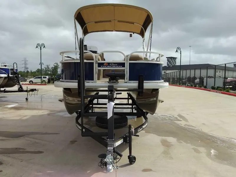 Slide: The Image of 2025 Sun Tracker Bass Buggy 18 DLX pontoon boat on trailer, outdoor display. - 2