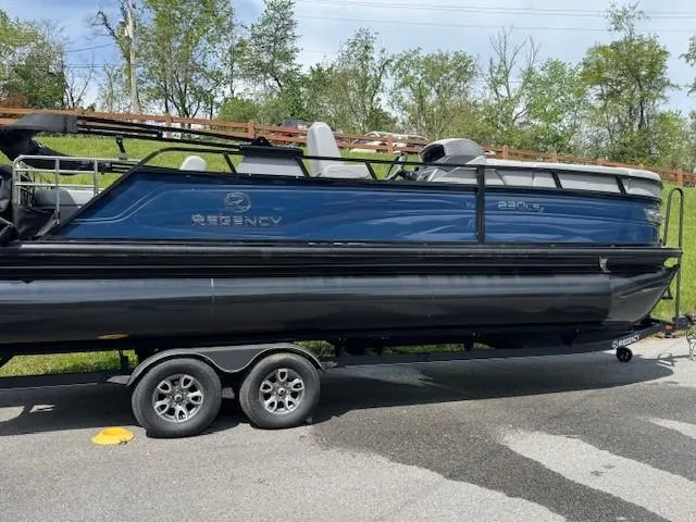 The Image of 2025 Regency 230 LE3 Sport pontoon boat on trailer, parked outdoors. - 0