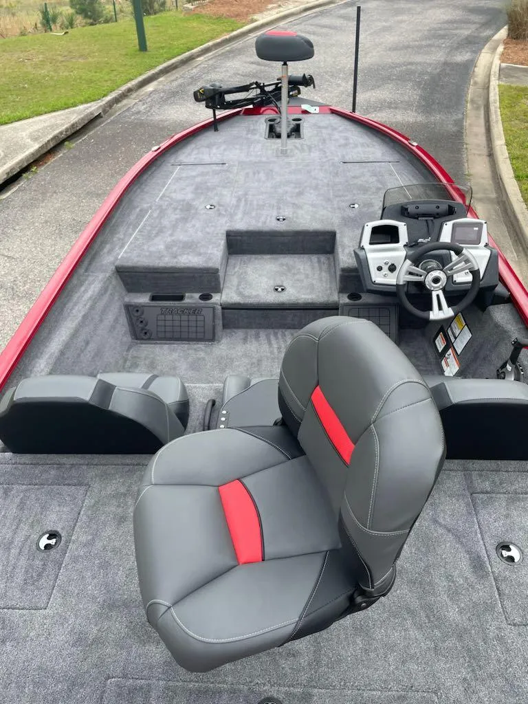 Slide: The Image of 2025 Tracker Savage 215 boat interior with gray and red seating, steering console, and fishing equipment. - 2