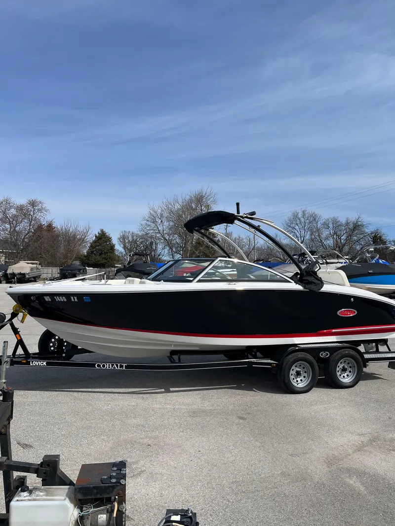 Slide: The Image of 2022 Cobalt CS23 boat on trailer, black and white design, parked outdoors. - 2