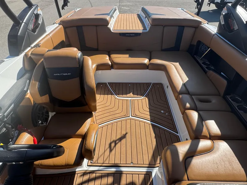 Slide: The Image of 2016 Nautique 210 boat interior with tan leather seats and wood-patterned flooring. - 10
