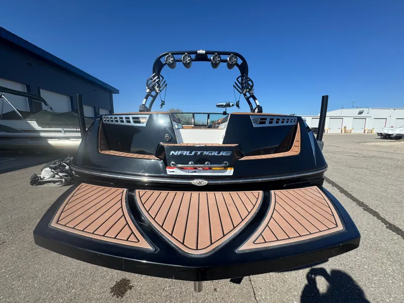 Slide: The Image of 2016 Nautique 210 boat, black with wood accents, parked outdoors under clear blue sky. - 16