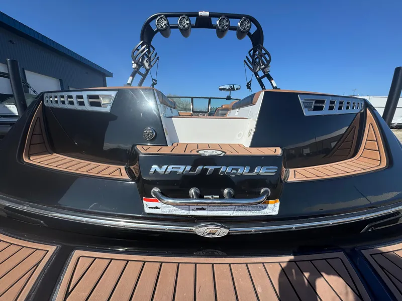 Slide: The Image of 2016 Nautique 210 boat rear view with teak deck and wakeboard tower. - 17