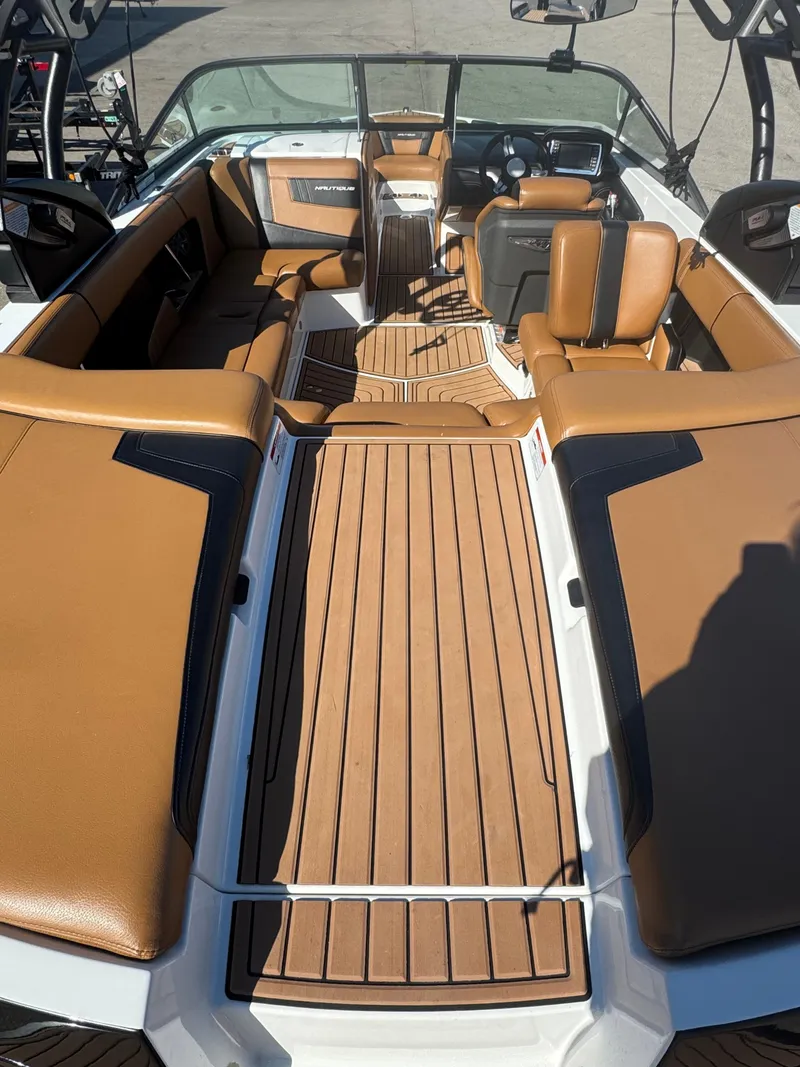 Slide: The Image of 2016 Nautique 210 boat interior with tan seating and wood-style flooring. - 21