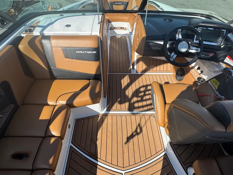 Slide: The Image of 2016 Nautique 210 boat interior with brown leather seats and wood-style flooring. - 28