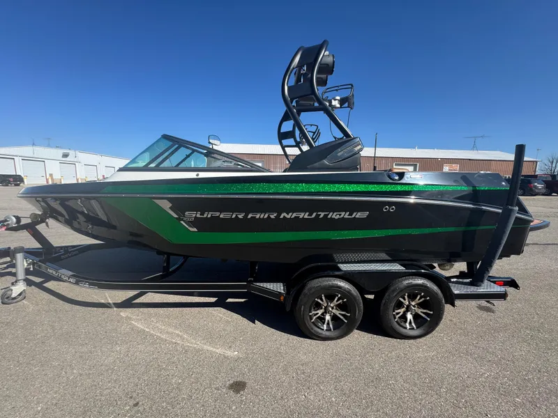 Slide: The Image of 2016 Nautique 210 boat with green accents on a trailer, parked outdoors. - 5