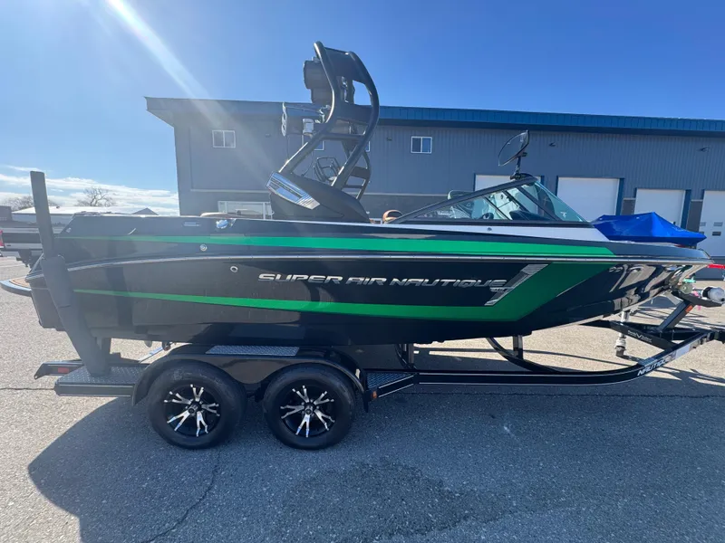 Slide: The Image of 2016 Nautique 210 boat on trailer, black and green, parked outdoors under clear sky. - 6