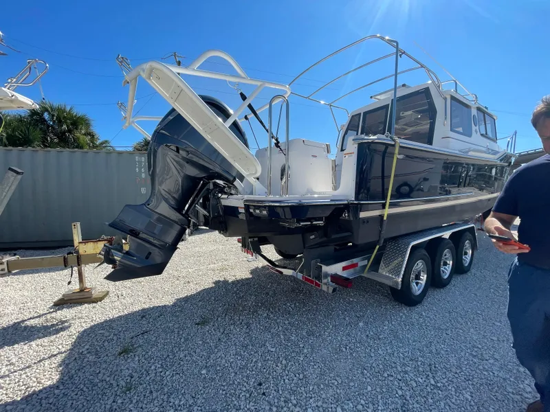 Slide: The Image of 2022 Ranger Tugs R-27 boat on a trailer, parked on gravel under a clear blue sky. - 0
