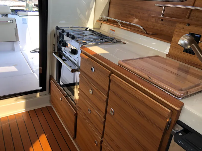 Slide: The Image of 2022 Ranger Tugs R-27 interior kitchen with stove, wooden cabinets, and cutting board. - 10