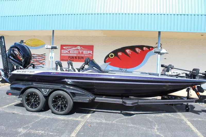 Slide: The Image of 2025 Skeeter FXR21L boat on trailer, parked outside a building with colorful mural. - 2