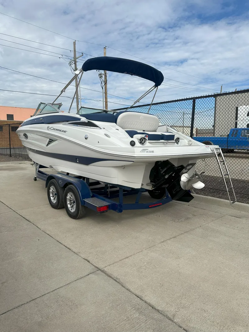 Slide: The Image of 2025 Crownline E235 boat on trailer, featuring sleek design and blue accents. - 2