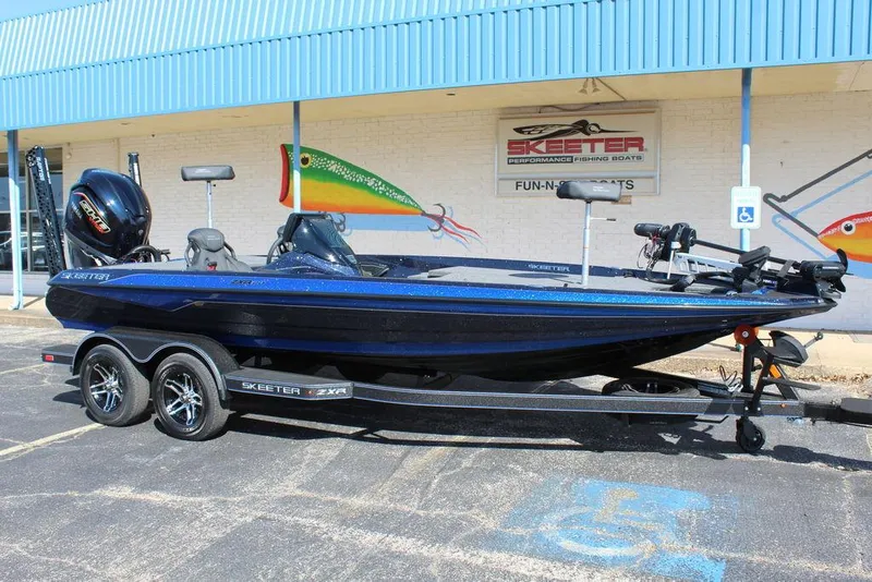 Slide: The Image of 2025 Skeeter ZXR20 boat on trailer, parked outside a dealership with fishing-themed murals. - 1