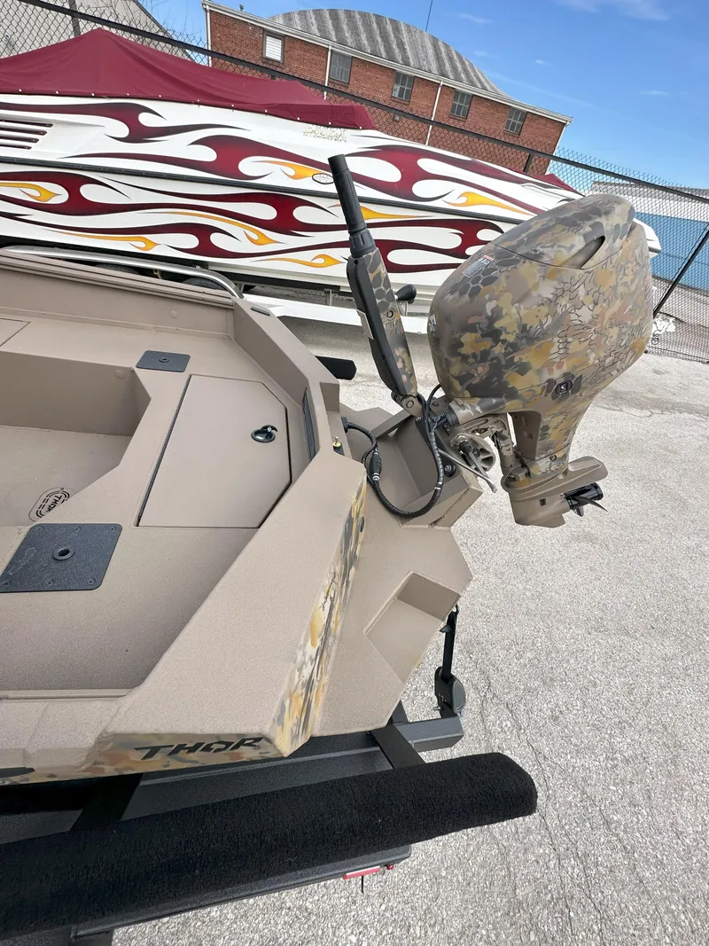Slide: The Image of 2025 Thor 1754 Timber Hammer boat with camo motor, parked near decorative wall. - 4