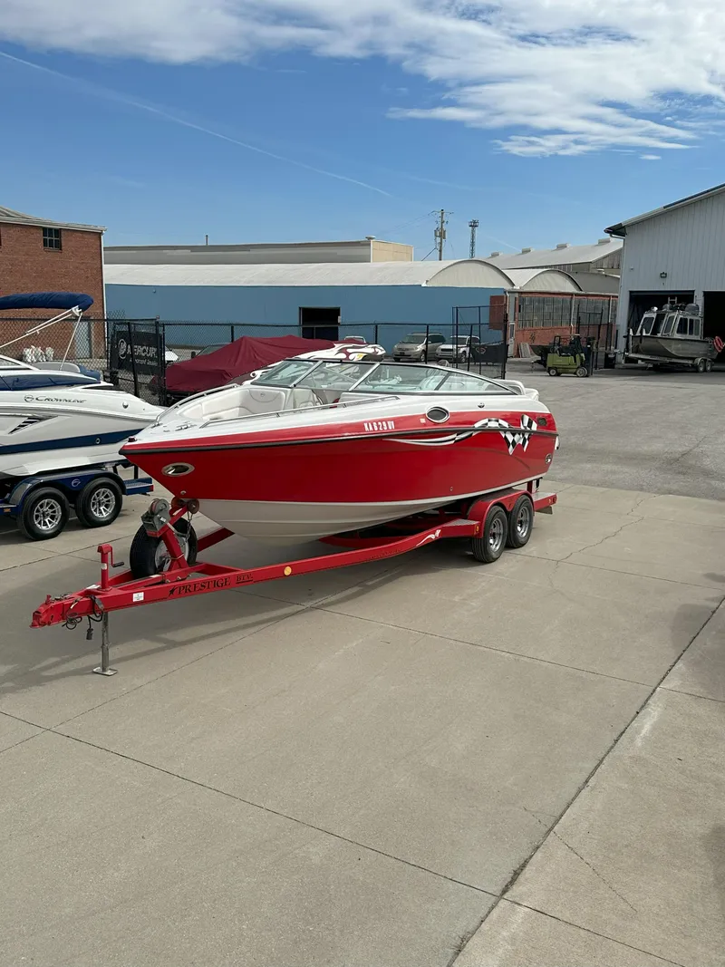 Slide: The Image of Red 2003 Crownline 230 boat on trailer, parked in a marina lot under a partly cloudy sky. - 0