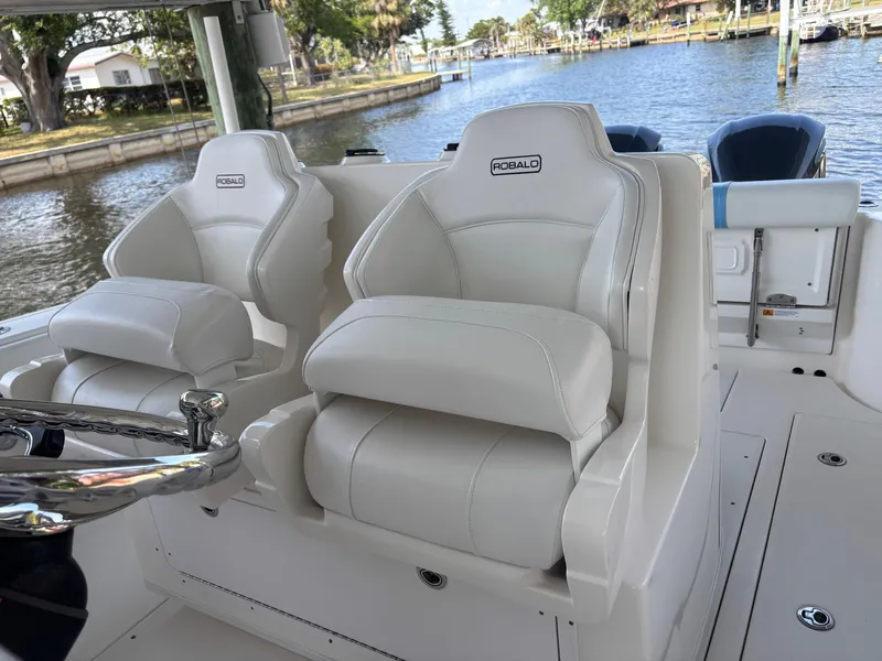 Slide: The Image of 2015 Robalo R300 Center Console boat with white cushioned seats by the water. - 11
