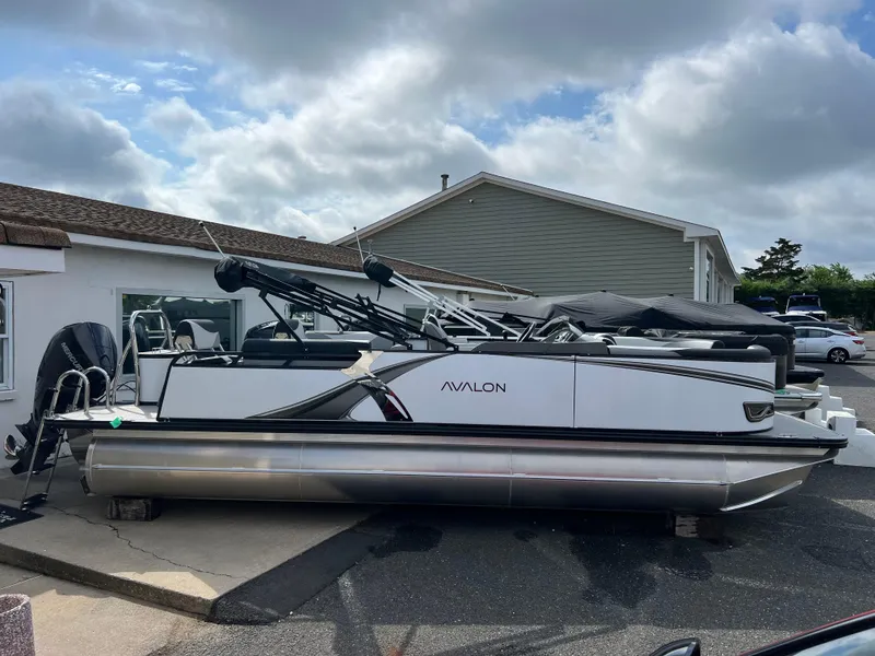 Slide: The Image of 2025 Avalon 2385 LSZ pontoon boat parked outside under cloudy sky. - 2