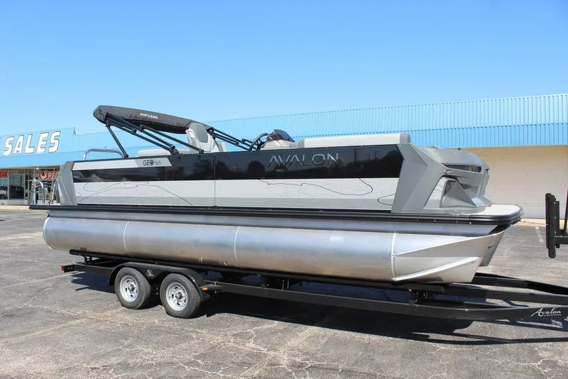 Slide: The Image of 2025 Avalon GEO FISH REAR FISH pontoon boat on trailer, parked outside sales building. - 3
