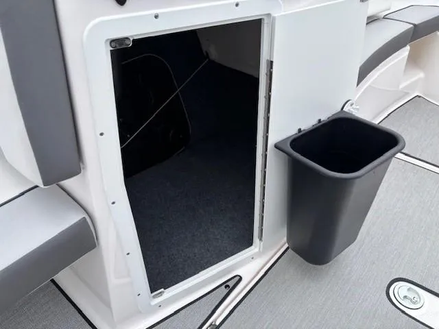 Slide: The Image of 2023 Yamaha Boats AR220 storage compartment with open door and attached trash bin. - 16