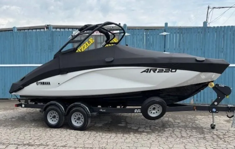 Slide: The Image of 2023 Yamaha Boats AR220 on trailer, covered, parked by blue fence. - 31
