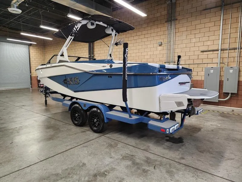 Slide: The Image of 2025 Axis T235 boat in a warehouse, featuring a blue and white design on a trailer. - 2