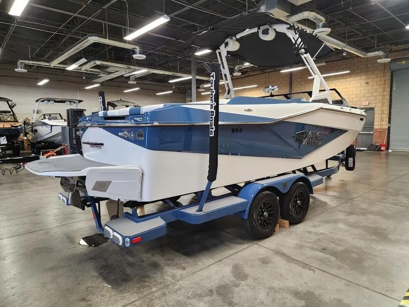 Slide: The Image of 2025 Axis T235 boat in a showroom, featuring a blue and white design on a trailer. - 5