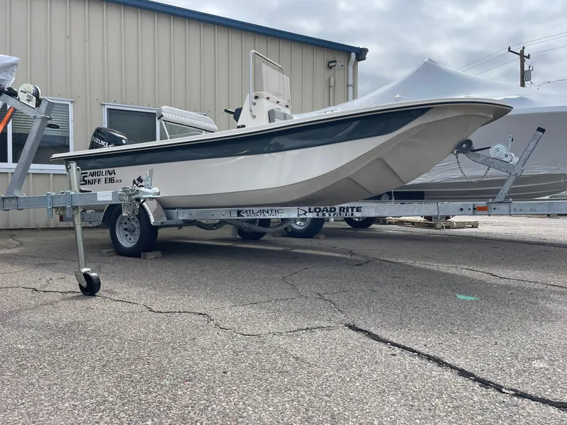 Slide: The Image of 2025 Carolina Skiff E16 JVX CC boat on trailer, parked outside a building. - 1