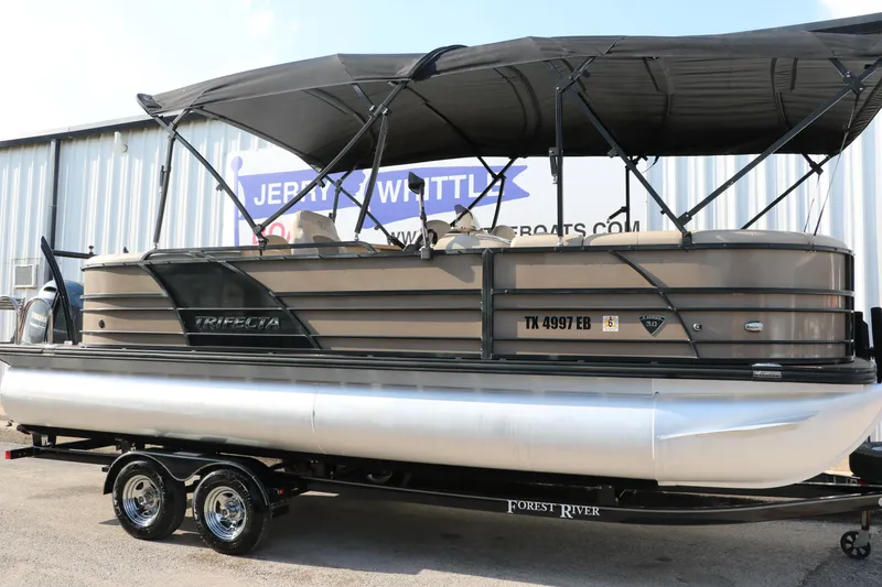 Slide: The Image of 2018 Trifecta 23 RFE pontoon boat with canopy on trailer, parked outside dealership. - 1