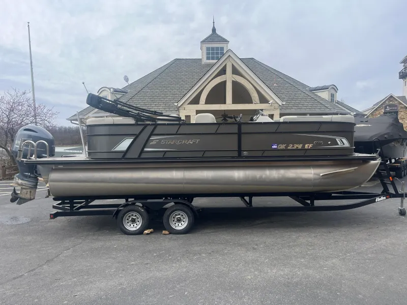 Slide: The Image of 2019 Starcraft EXS 3 pontoon boat on trailer, parked near a building. - 1