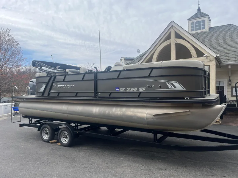 Slide: The Image of 2019 Starcraft EXS 3 pontoon boat on trailer, parked near a building. - 2