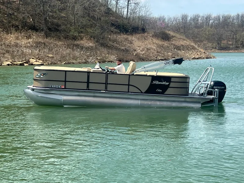 Slide: The Image of 2019 Bentley Pontoons 223 on a serene lake with a scenic backdrop. - 2