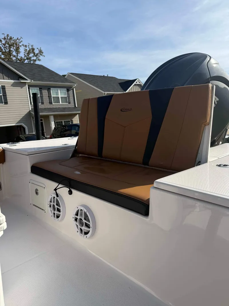 Slide: The Image of 2024 Robalo 226 Cayman boat with brown seating and dual speakers, parked in a residential area. - 7