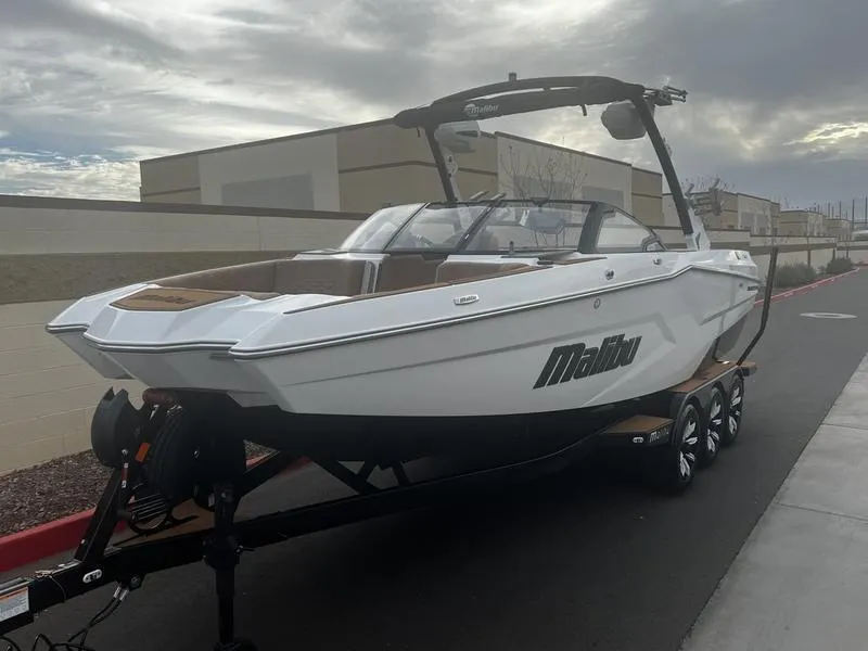 Slide: The Image of 2025 Malibu 24 MXZ boat on trailer, sleek design, white exterior, overcast sky. - 2