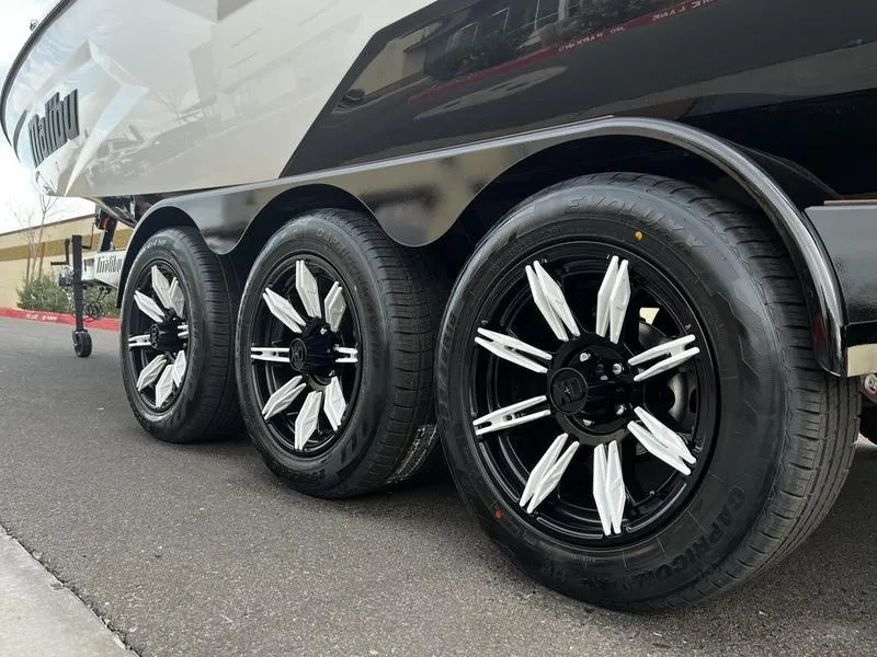 Slide: The Image of 2025 Malibu 24 MXZ trailer with stylish black and white wheels on pavement. - 7