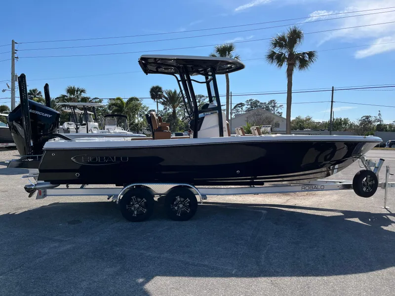 Slide: The Image of 2025 Robalo 246 Cayman boat on trailer, parked outdoors under clear sky. - 0