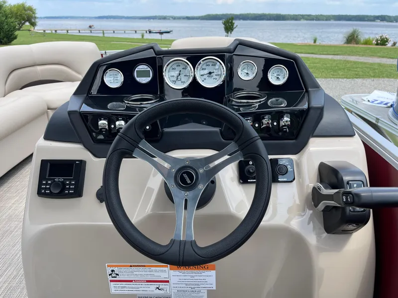 Slide: The Image of 2024 Landau Island Breeze 232 Cruise dashboard with steering wheel and gauges, overlooking a scenic lake. - 6