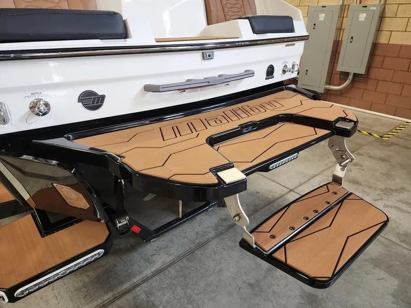 Slide: The Image of 2025 Malibu 24 MXZ boat with teak swim platform and step ladder in a garage setting. - 21