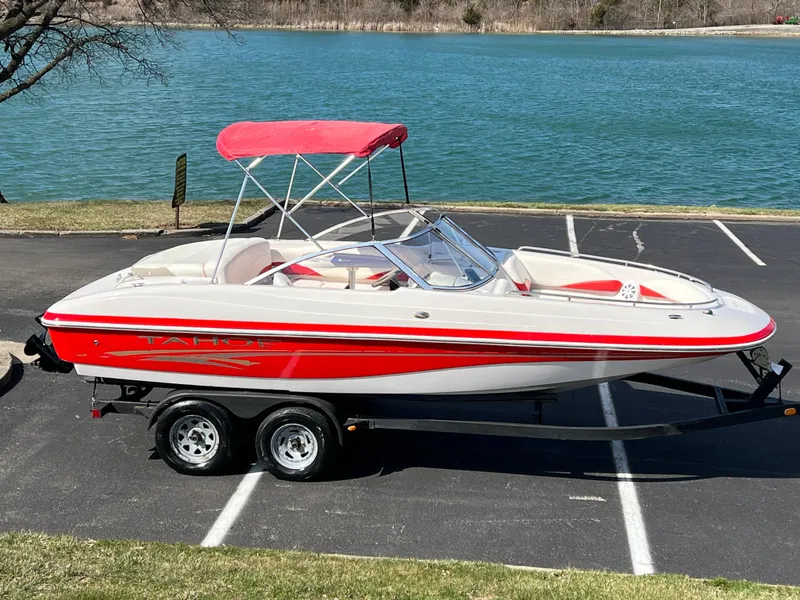 Slide: The Image of 2006 Tahoe 204 WT boat with red accents and canopy, parked near a lake. - 1