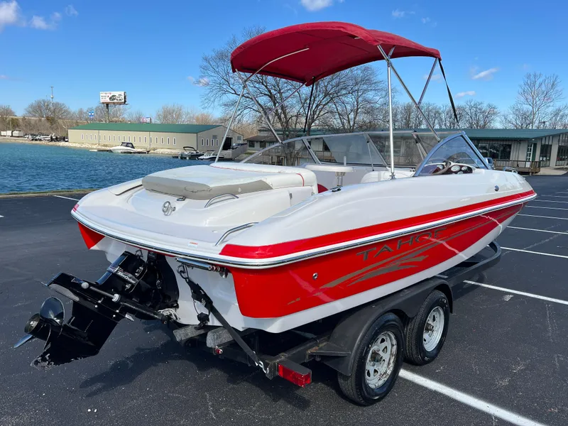 Slide: The Image of 2006 Tahoe 204 WT boat with red accents and canopy on a trailer by the water. - 5
