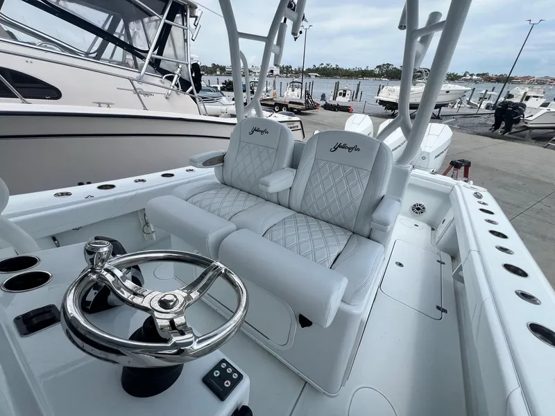 Slide: The Image of 2021 Yellowfin 36 Offshore boat interior with white seating and steering wheel at a marina. - 33