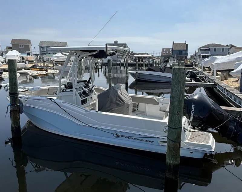Slide: The Image of 2022 Finseeker 230 CC boat docked in a marina, surrounded by other boats and waterfront homes. - 2