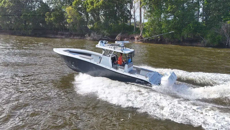 Slide: The Image of 2022 Yellowfin 34 boat cruising on a river with lush green trees in the background. - 12