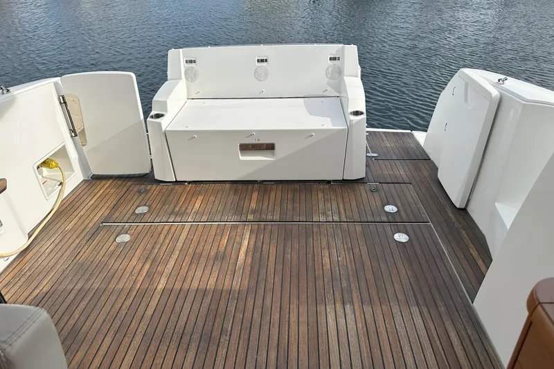 Slide: The Image of 2016 Jeanneau NC 11 boat deck with wooden flooring and white seating, overlooking water. - 19