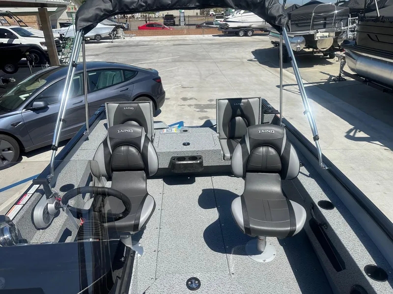 Slide: The Image of 2025 Lund Adventure 1675 SS boat interior with seating and steering wheel, parked outdoors. - 12