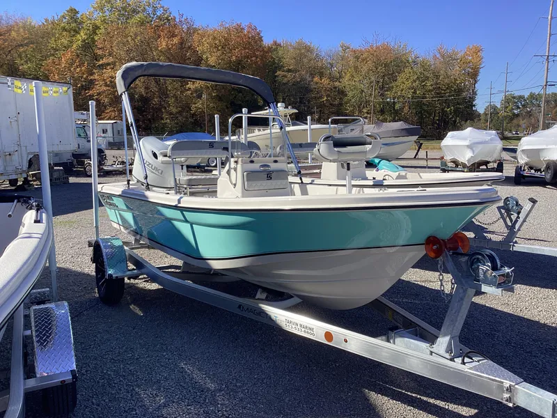 Slide: The Image of 2025 Carolina Skiff 178 JLS boat on trailer, parked outdoors with trees in background. - 10