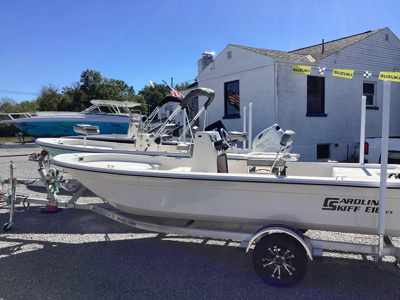 Slide: The Image of 2025 Carolina Skiff E18 JVX CC boat on trailer, parked outdoors near building. - 10
