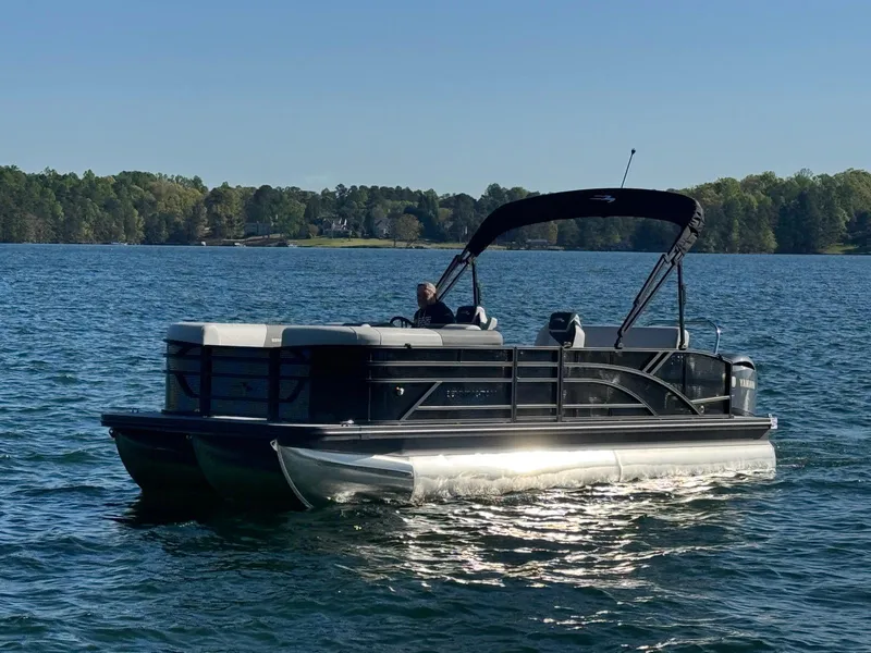 Slide: The Image of 2025 Bennington 22SSB pontoon boat cruising on a serene lake under clear skies. - 1